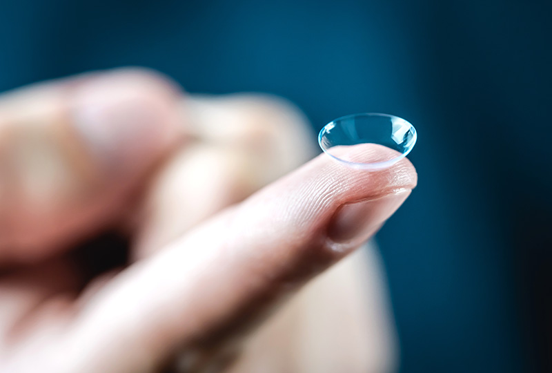 Eine Kontaktlinse wird auf einem Zeigefinger vor blauem Hintergrund gehalten